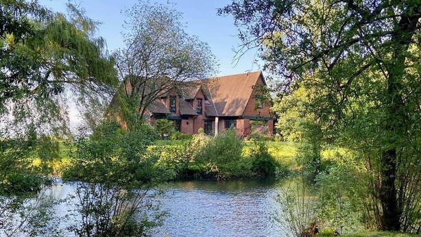 A large brick building with a sloped roof, surrounded by lush greenery and a body of water. - The Saint-Josse Tribe (Saint-Josse)
