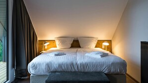 A bedroom with a large bed, two bedside lamps, and a window with curtains.