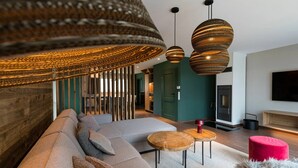 A modern living room with a large sectional sofa, two wooden side tables, a red ottoman, and a large woven pendant light fixture.