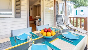 Zona pranzo all'aperto con tavolo imbandito per due, una ciotola di frutta e una sedia con chaise longue.
