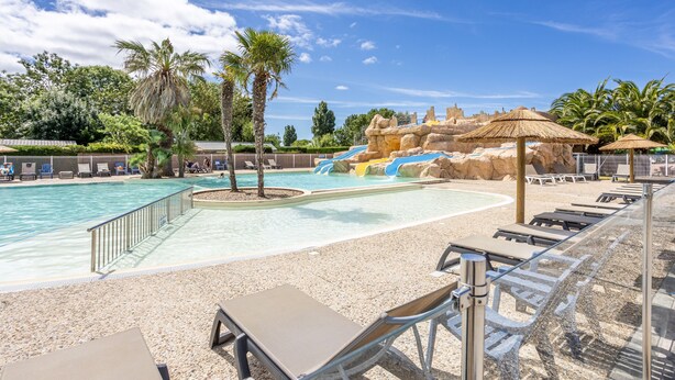 Una piscina con lettini, palme e uno scivolo.