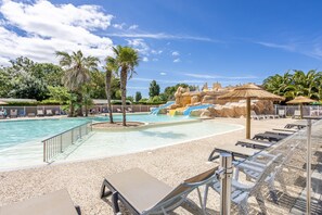A swimming pool with lounge chairs, palm trees, and a water slide. - Mobile Home 'Ile D'Oleron' with Shared Pool, Private Terrace and Garden (Saint-denis-D'oleron)