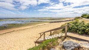 Una spiaggia sabbiosa con una scala di legno che scende verso l'acqua, un litorale roccioso e un cielo sereno.