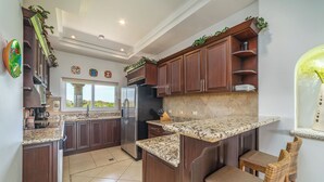 A kitchen with dark wood cabinets, granite countertops, and a built-in island with seating. - Matapalo 503, beautiful Oceanview Condo with Giant Pool (Tamarindo)