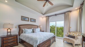 A bedroom with a large bed, a nightstand, a chair, and a view of the outdoors. - Matapalo 503, beautiful Oceanview Condo with Giant Pool (Tamarindo)