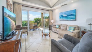 A spacious living room with a large TV, comfortable seating, a ceiling fan, and a view through the glass doors. - Matapalo 503, beautiful Oceanview Condo with Giant Pool (Tamarindo)