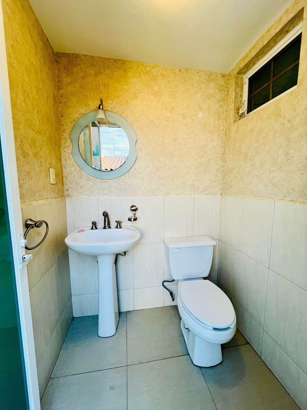 Un baño pequeño con lavamanos, inodoro y un espejo redondo en la pared.