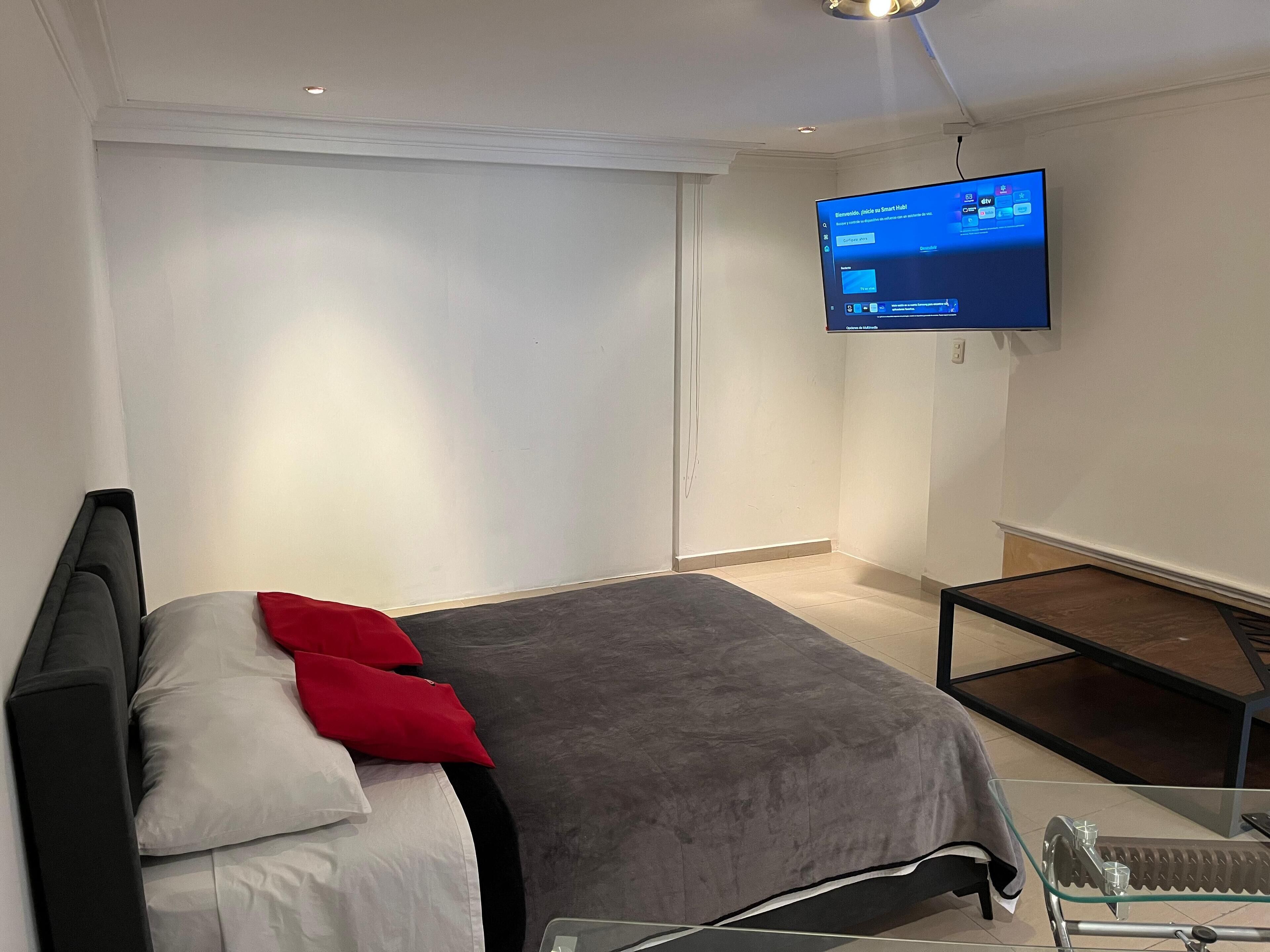 Une chambre d’hôtel moderne avec un lit, un téléviseur fixé au mur et une petite table.