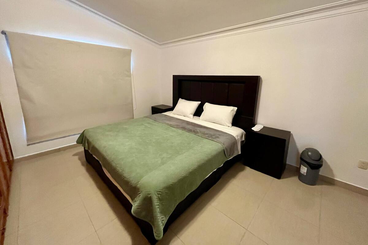 A neatly arranged bedroom with a bed, bedside tables, and a trash bin.