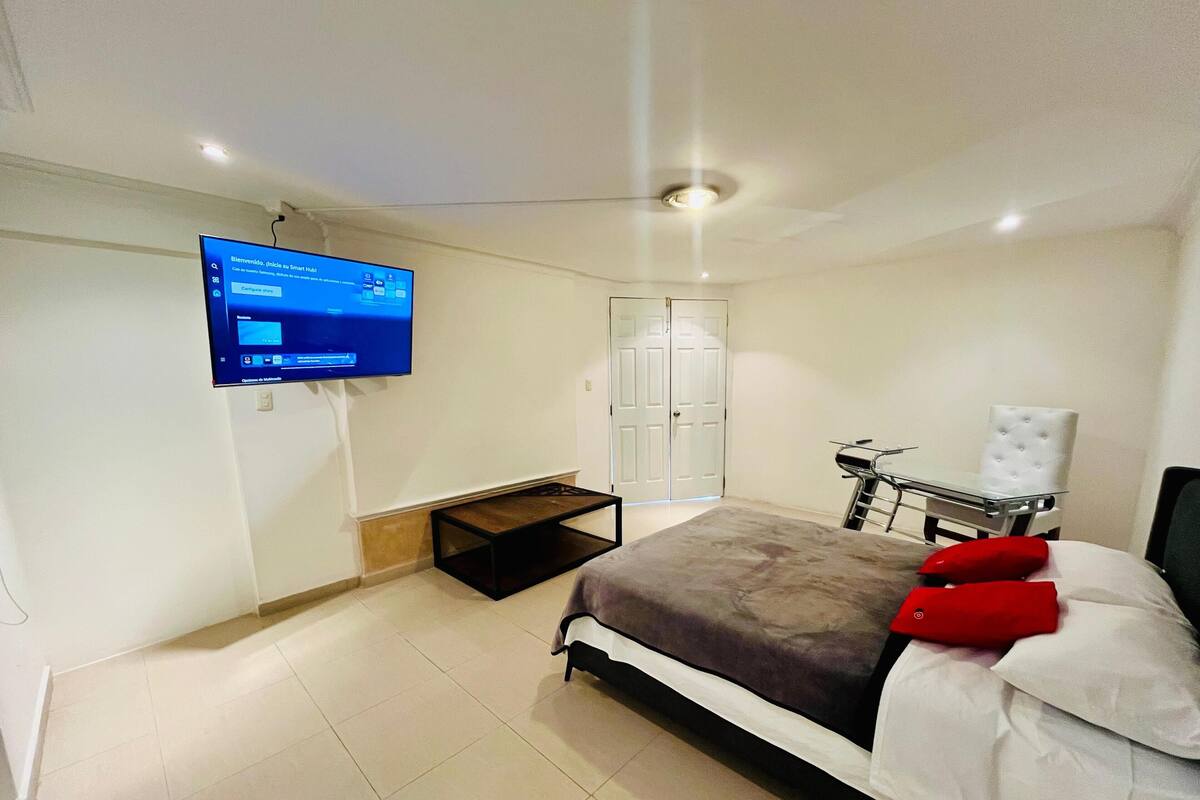 A bedroom with a bed, a TV mounted on the wall, a wardrobe, and a small table.