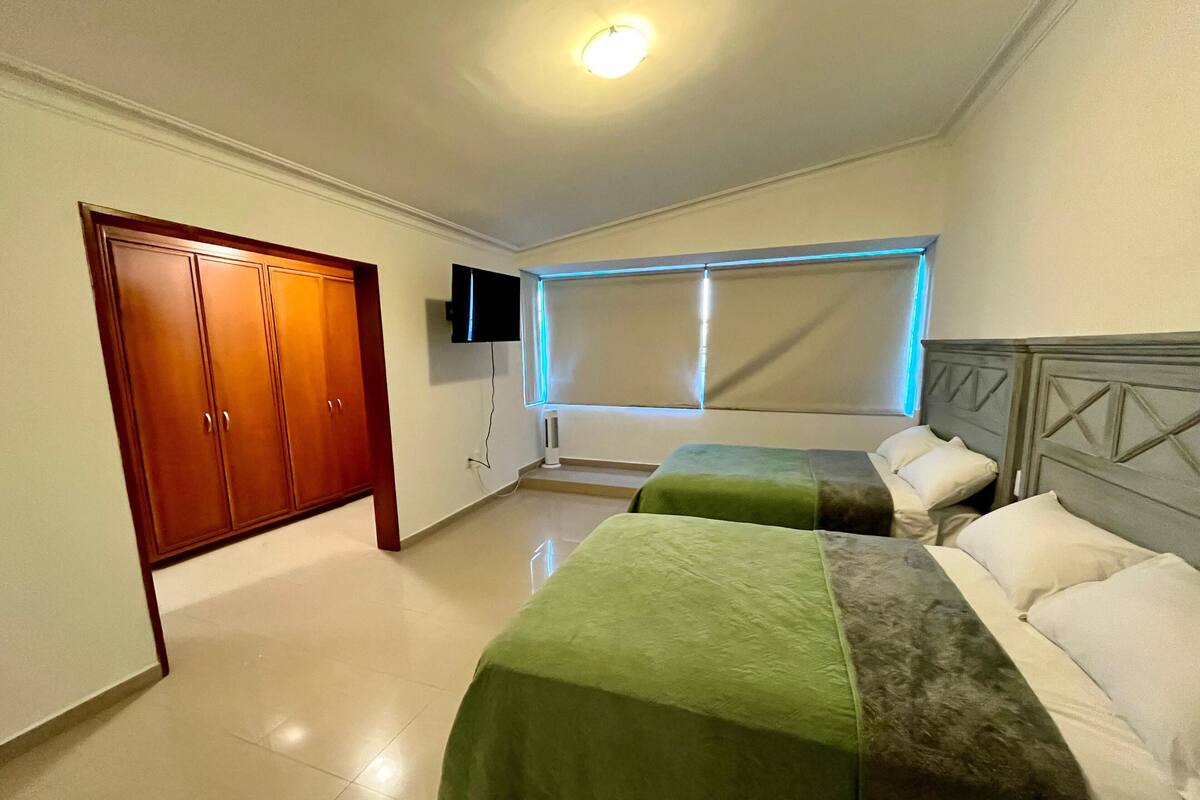 A hotel room with two beds, a wardrobe, a TV, and a window with blinds.
