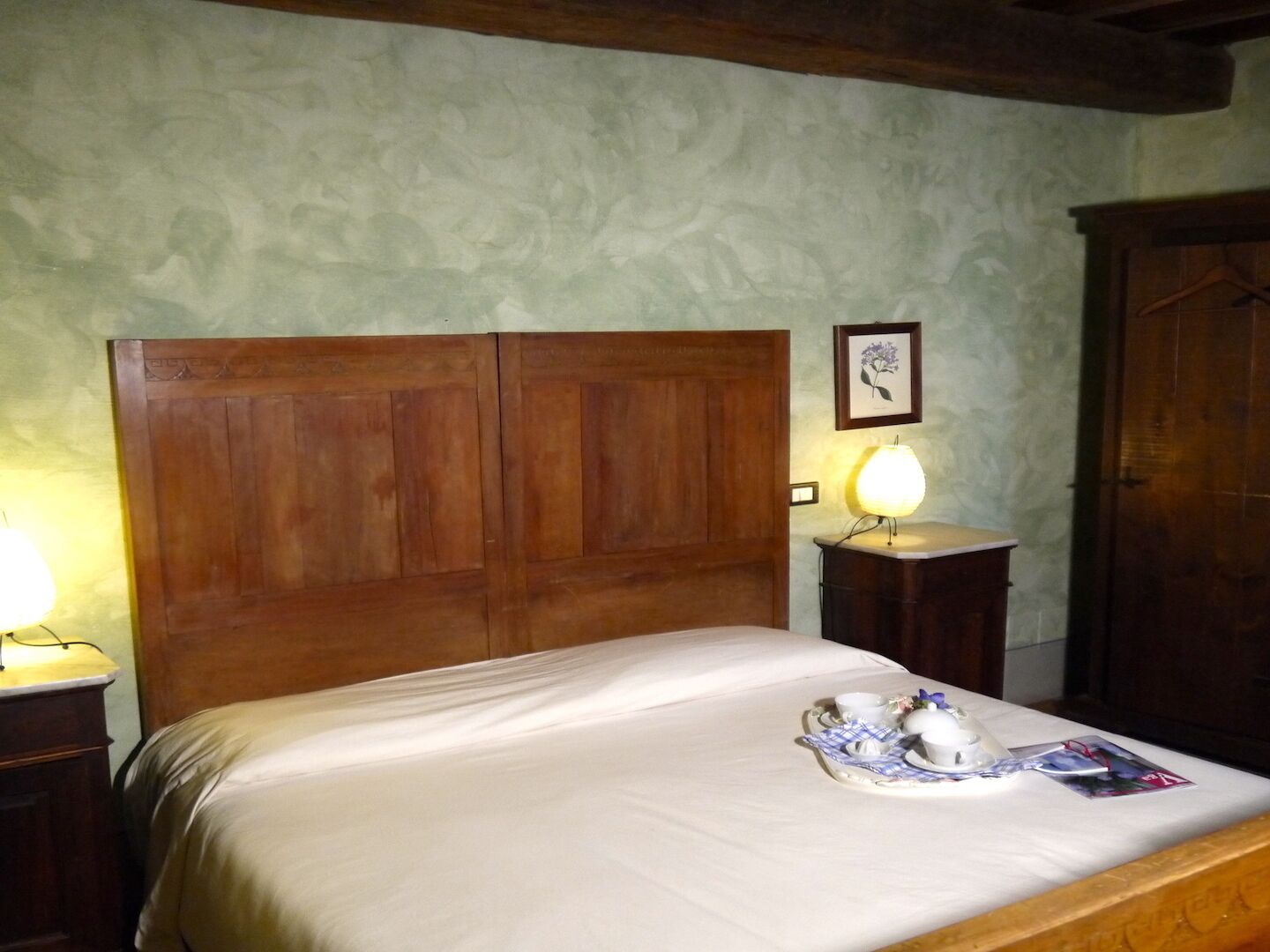 A room with a wooden bed, a bedside table with a lamp, and a framed picture on the wall.