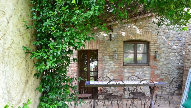 Une terrasse extérieure avec un mur en pierre, une table entourée de chaises en métal et une fenêtre.