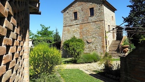 Une tour de pierre dotée d’une petite fenêtre et d’une porte, entourée d’un jardin où poussent des fleurs jaunes et bordée d’un mur de briques.