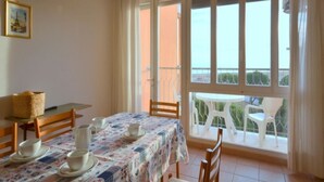 A dining area with a table set for four, a chair, a small table with a basket, and a view of the outside through a glass door.