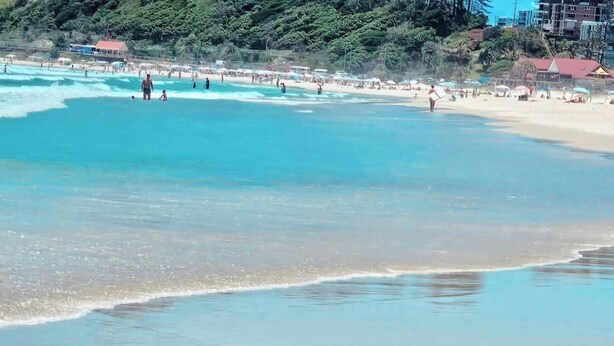 A beach with clear turquoise water, a sandy shore, and buildings in the background. - Bask in Beach Luxury! (Coolangatta)