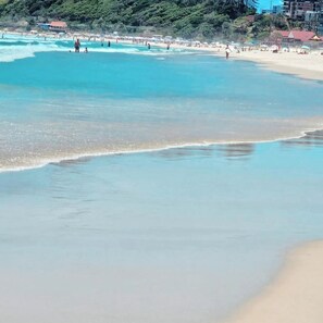A beach with clear turquoise water, a sandy shore, and buildings in the background. - Bask in Beach Luxury! (Coolangatta)