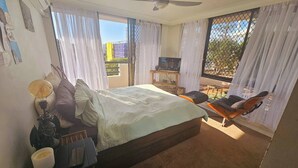 A bedroom with a bed, a TV, a chair, and a balcony with a view. - Bask in Beach Luxury! (Coolangatta)