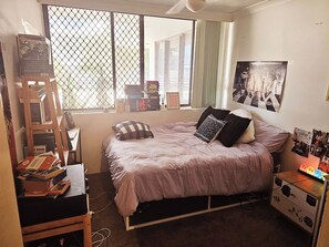 Un dormitorio con cama, escritorio, escalera, ventana con vistas y pared con un cartel.
