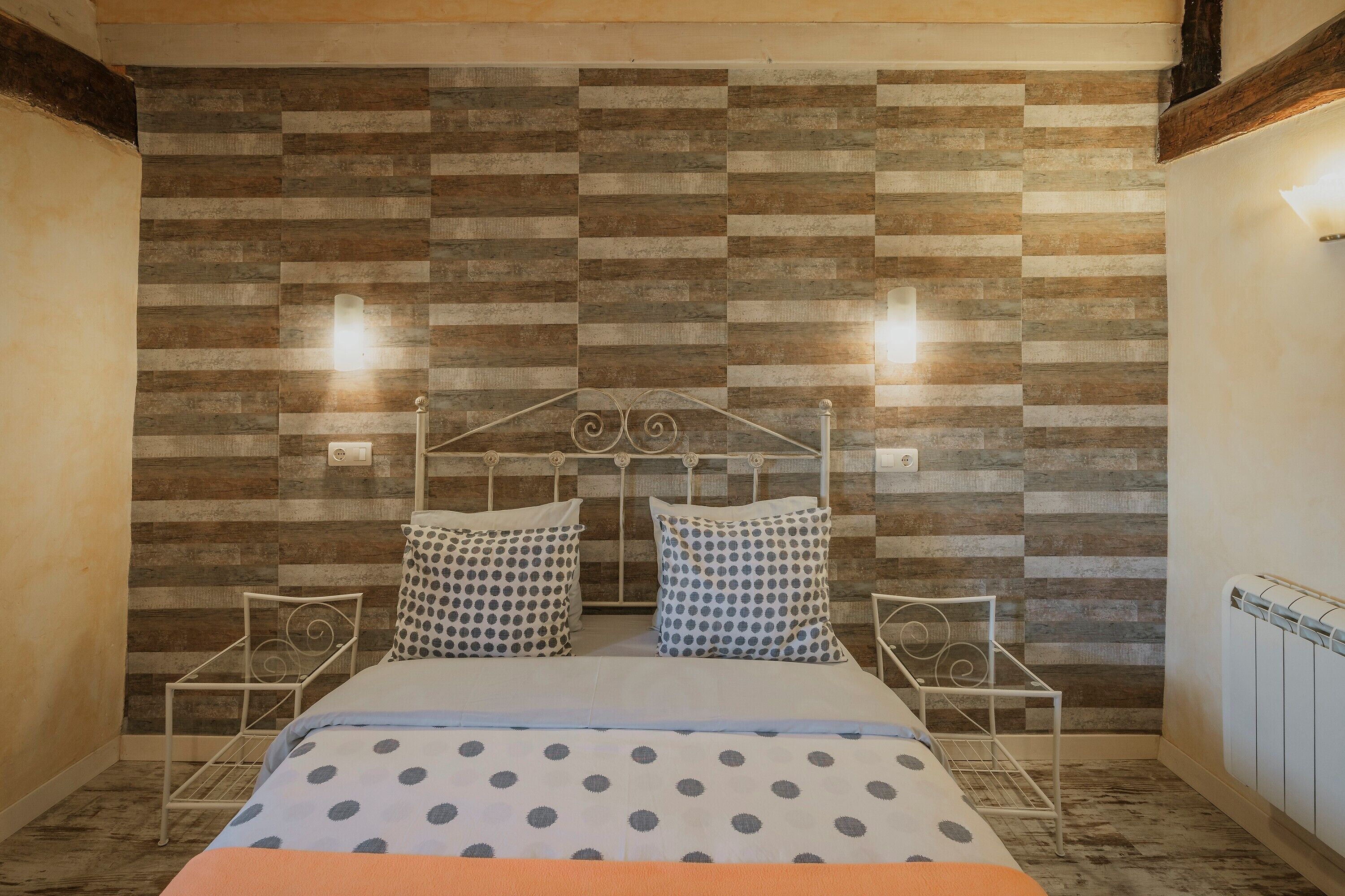 A bedroom with a bed, two bedside tables, a radiator, and a wall with a wooden panel design.