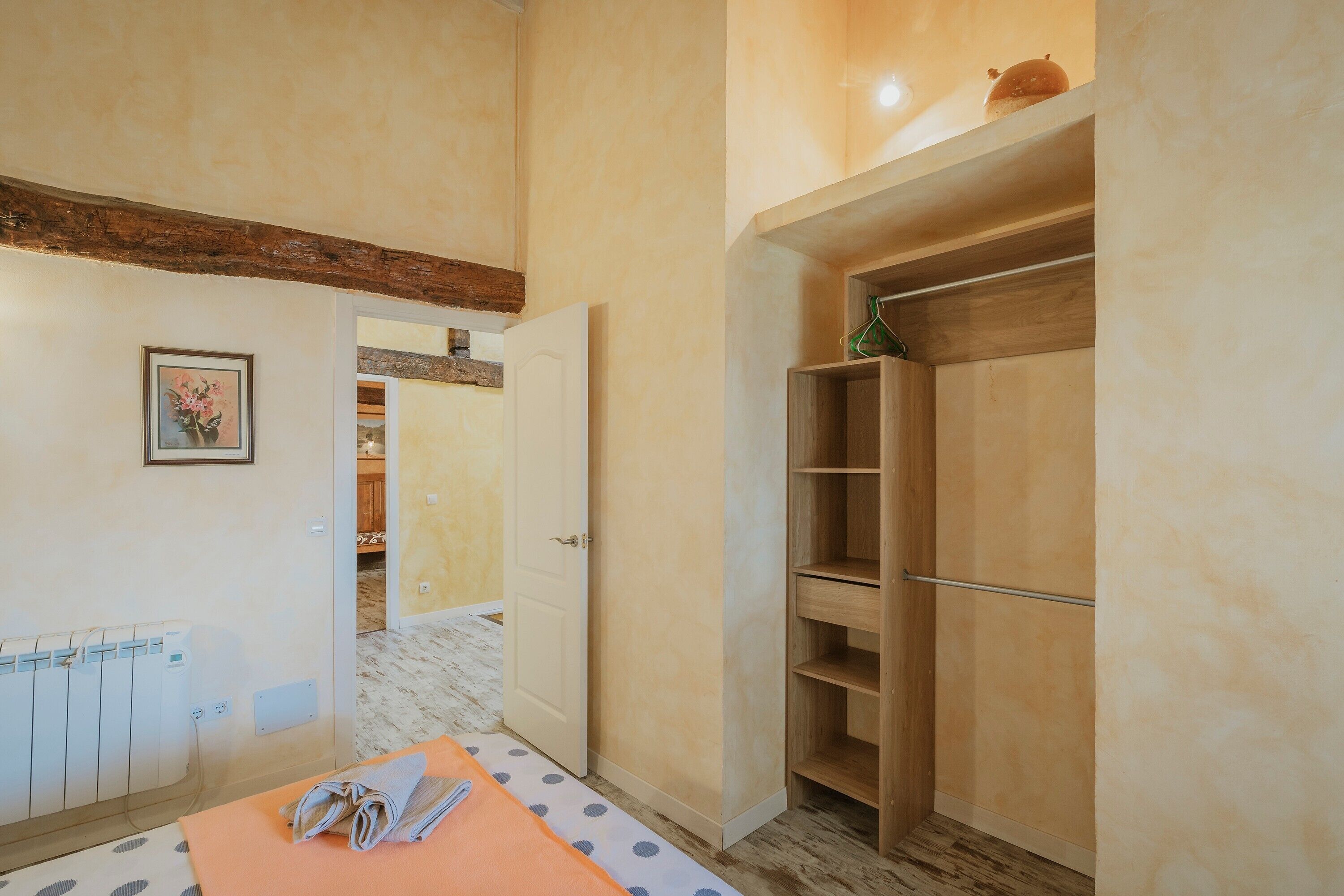A room with a bed, a wooden wardrobe, a radiator, and a door leading to another room.