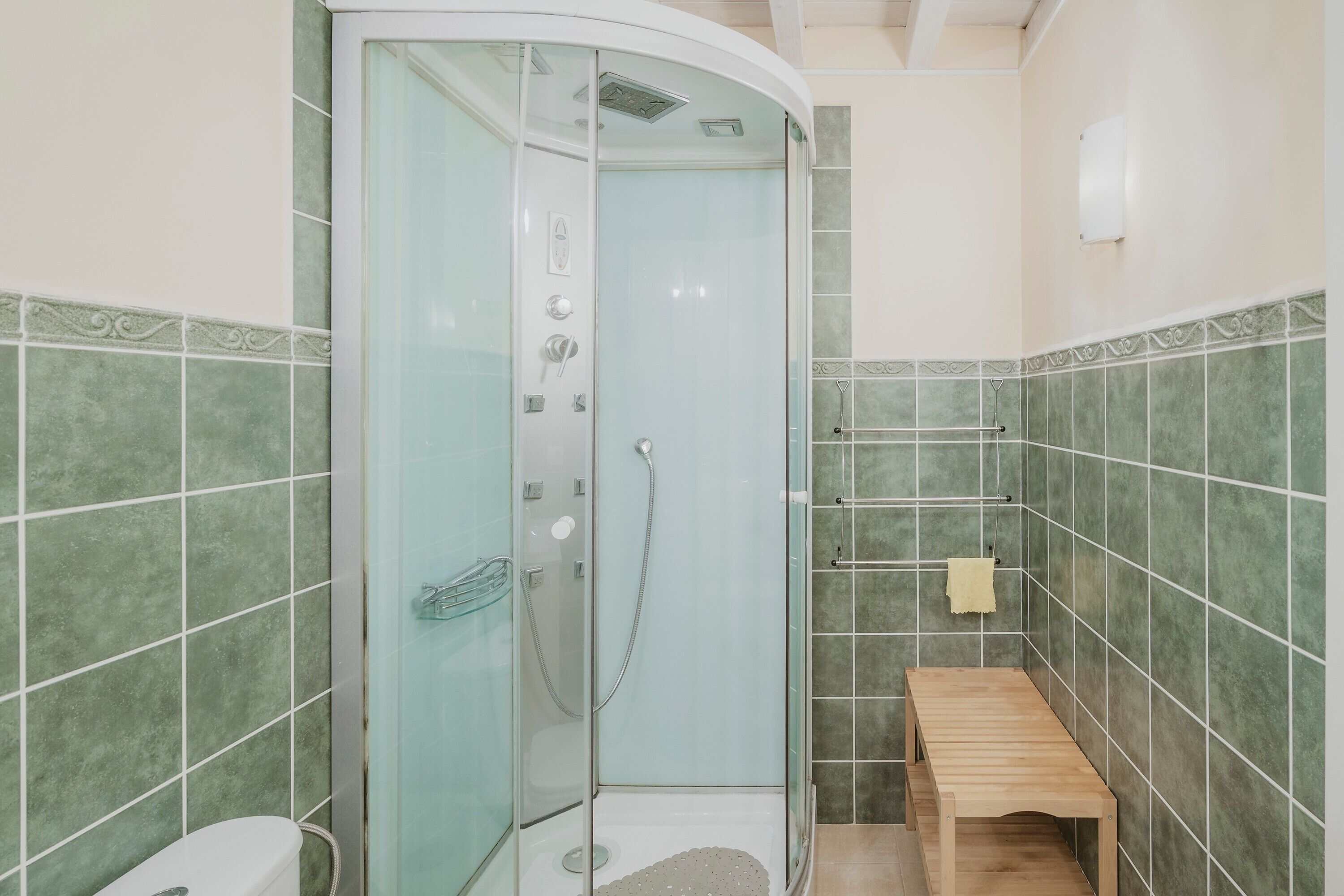 A bathroom with a glass-enclosed shower, a wooden bench, and tiled walls.