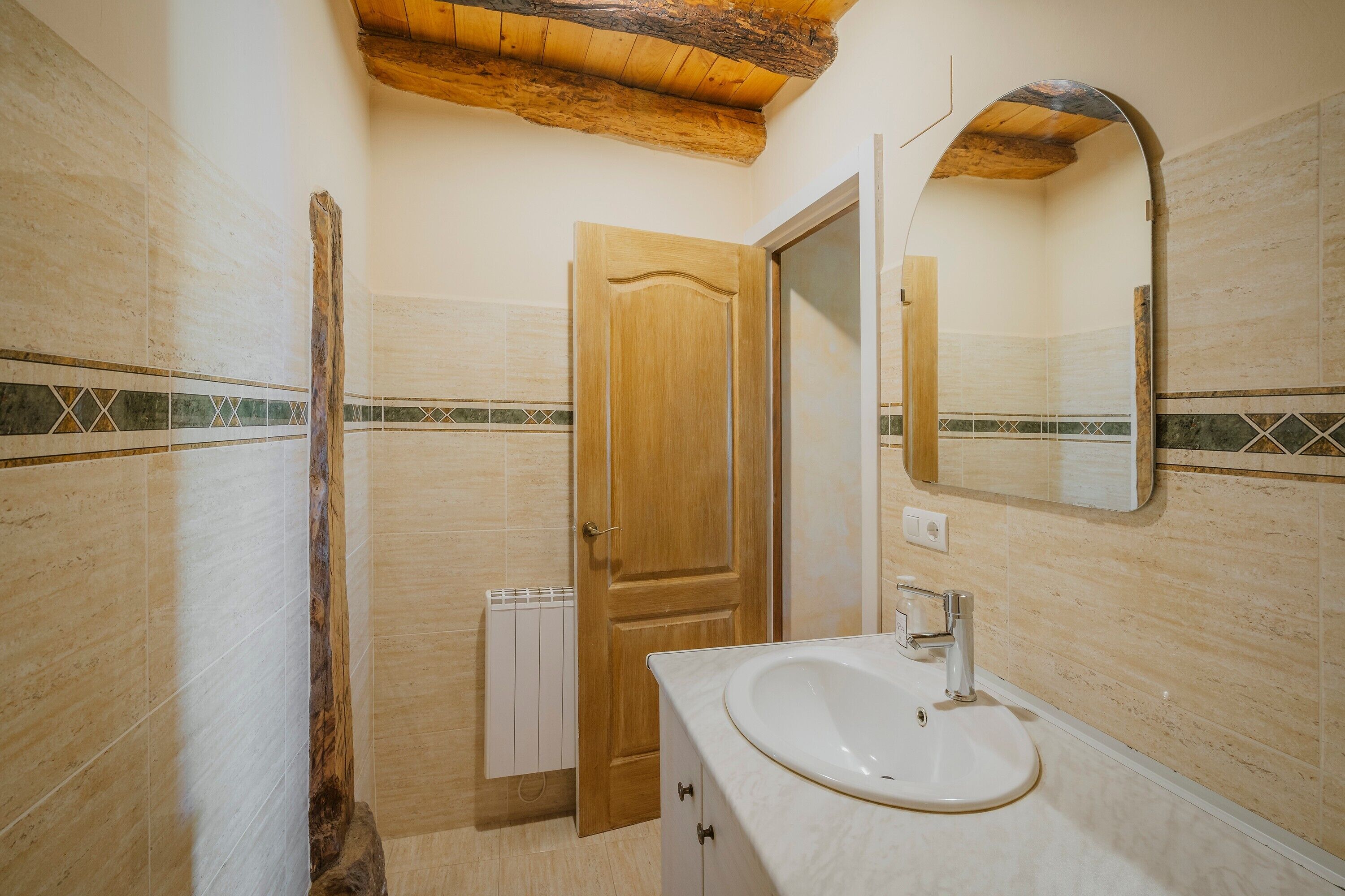 Une salle de bain avec une porte en bois, un lavabo blanc, un miroir et des murs carrelés.