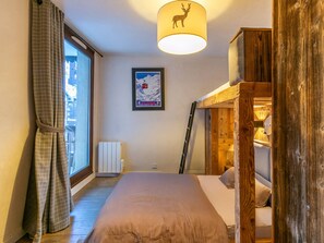 A bedroom with a bed, a window with curtains, a radiator, a framed picture on the wall, and a wooden structure with a lamp.