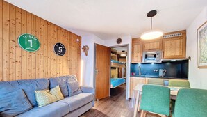 Ein gemütlicher, kleiner Wohnraum mit einer Couch, einem Esstisch mit Stühlen, einer Küchenzeile und einer Holzwand mit Schildern.