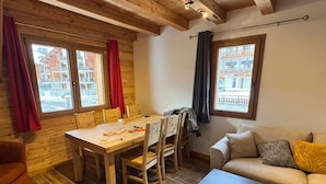 A cozy room with a wooden dining table, chairs, a sofa, and a window with a view of buildings.