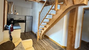A compact kitchen with modern appliances, a wooden staircase, and a cozy seating area with a hat and blanket.