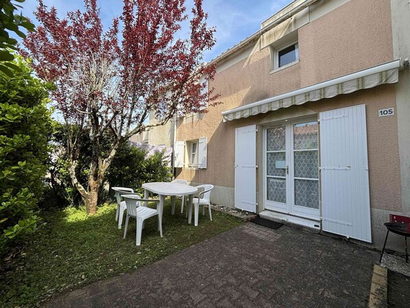 A residential building with a number 105, a small patio with a table and chairs, and a tree with red leaves.