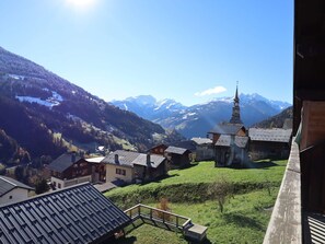A village with traditional wooden houses, a church with a tall steeple, and snow-capped mountains in the background. - Charming T3 with pool and balcony, near slopes (Hauteluce)