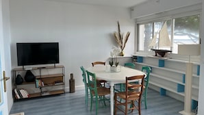 A dining area with a white table, green chairs, a TV, and a bookshelf. - Seafront T3 apartment with secure parking and WiFi (Arcachon)