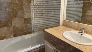 A bathroom with a bathtub, a sink, and a patterned wall. - Seafront T3 apartment with secure parking and WiFi (Arcachon)