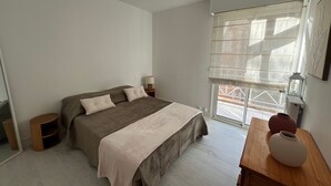A bedroom with a bed, bedside tables, a window with blinds, and a wooden nightstand. - Seafront T3 apartment with secure parking and WiFi (Arcachon)