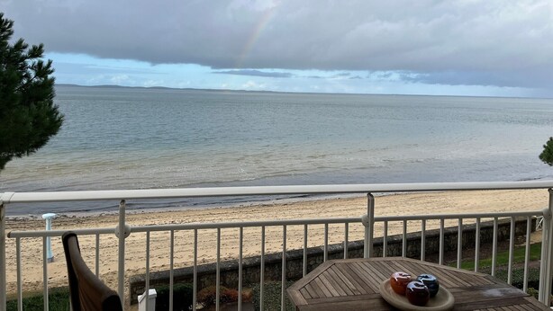 A balcony with a view of the beach and ocean, a wooden table with decorative items, and a railing. - Seafront T3 apartment with secure parking and WiFi (Arcachon)