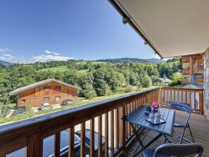 Enjoy a serene mountain view from this balcony with a table, chairs, and a potted plant.