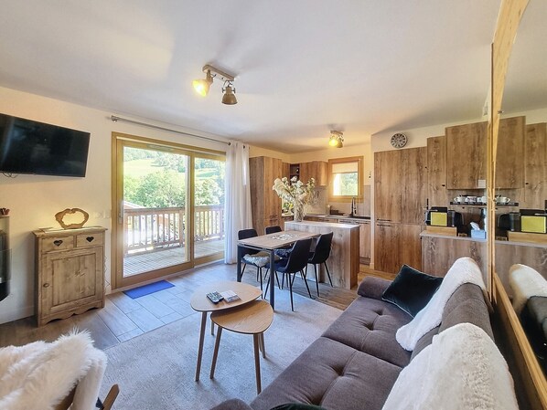 Relax in a spacious living area with a sofa, TV, and balcony overlooking lush greenery.