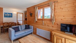 Interior acogedor de una cabaña con sofá, mesa de comedor de madera, televisor y ventana con cortinas.