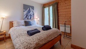 Un dormitorio con cama de madera, un cuadro de una montaña, dos lámparas de noche y una ventana con cortinas.