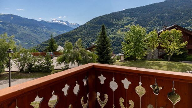 Un balcón de madera con vistas a un paisaje montañoso, que incluye una casa y una colina boscosa.