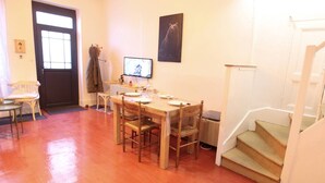 A dining area with a wooden table and chairs, a television, and a staircase leading to an upper floor.