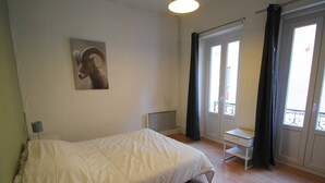 A bedroom with a bed, a desk, a chair, a lamp, a radiator, and a window with curtains.