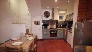 A compact kitchen with a dining area, a clock, and a refrigerator.