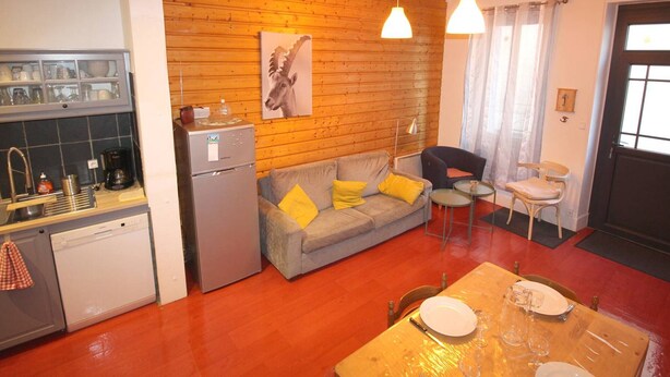 A compact living space with a kitchenette, a sofa with yellow cushions, a dining table with plates, and a wooden wall with a moose painting.
