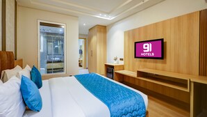 A hotel room with a bed, a TV mounted on the wall, and a wooden wardrobe. - Hotel 91 Huda Premier (Gurugram)