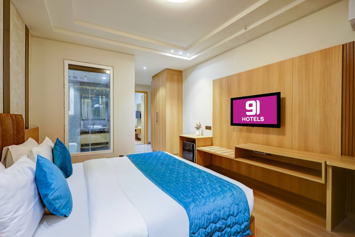A hotel room with a bed, a TV mounted on the wall, and a wooden wardrobe.