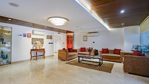 A spacious living area with a wooden ceiling, a marble floor, and multiple sofas with red cushions. - Hotel 91 Huda Premier (Gurugram)