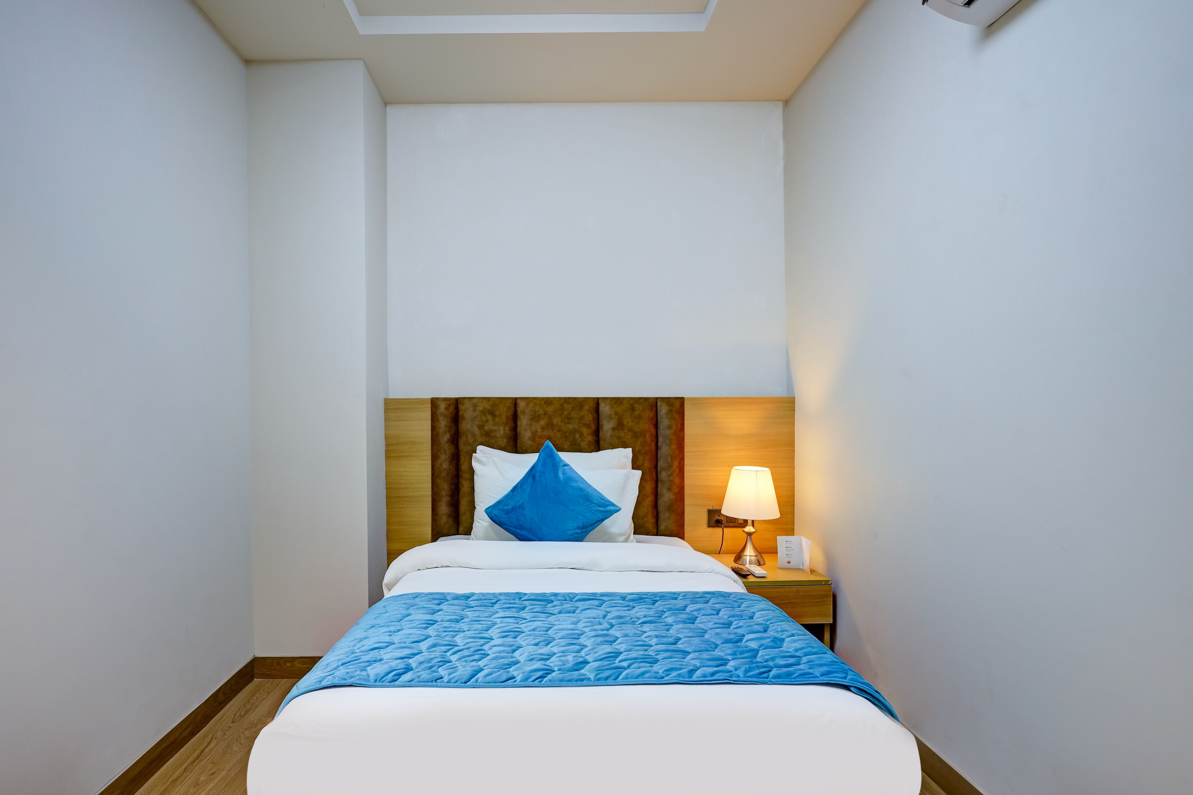 A hotel room with a bed, a nightstand, a lamp, and a wooden headboard.